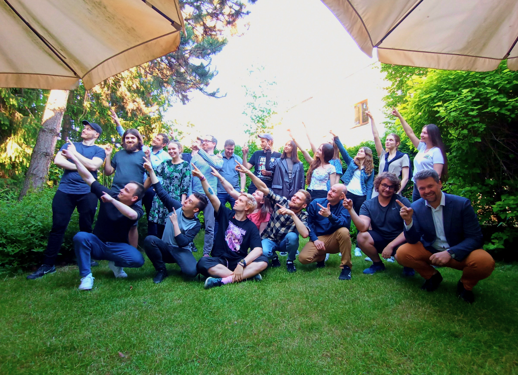 A group of over 20 smiling team members, posing together in a garden, all pointing in the same direction